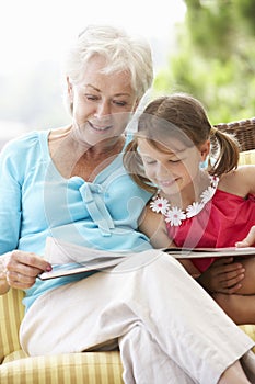 Grandmother And Granddaughter Reading Book On Garden Seat