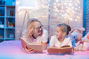 Grandmother and granddaughter are reading books before sleep at night at home.