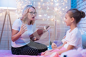 Grandmother and granddaughter are reading children`s book at night at home.