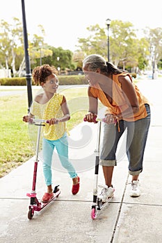 Grandmother And Granddaughter Riding Scooters In Park