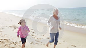 Grandmother And Granddaughter Running Along Beach Together