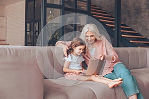 Grandmother and granddaughter sitting on the couch and using laptop at home