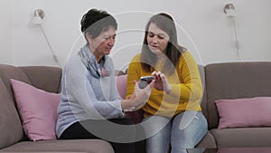 Grandmother and granddaughter sitting on a couch, young woman teaching her grandmother how to send a text message