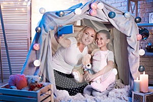 Grandmother and granddaughter are taking selfie in blanket house at night at home.