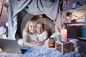 Grandmother and granddaughter are talking to family on laptop in blanket house at night at home.