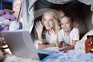 Grandmother and granddaughter are talking to family on laptop in blanket house at night at home.