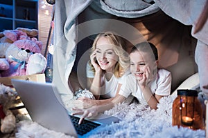 Grandmother and granddaughter are talking to family on laptop in blanket house at night at home.