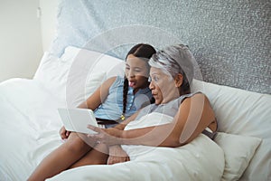 Grandmother and granddaughter using digital tablet in bed room