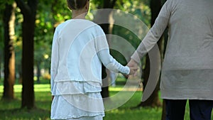Grandmother and granddaughter walking along park holding hands, happy family