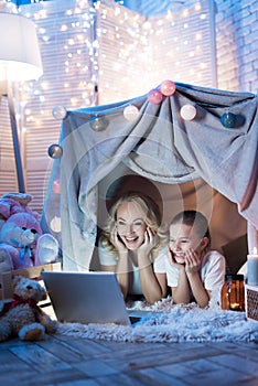 Grandmother and granddaughter are watching movie on laptop in blanket house at night at home.