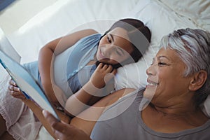 Grandmother and granddaughter watching photo album together in bed room