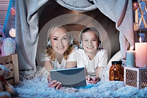 Grandmother and granddaughter are watching video on tablet in blanket house at night at home.