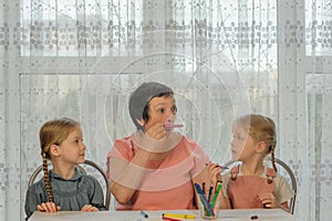 grandmother and granddaughters fooling around at home while drawing. grandma makes herself a mustache from a marker