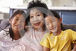 Grandmother And Granddaughters Relaxing On Sofa At Home