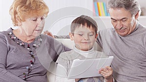 Grandmother , grandfather and grandson looking at digital tablet while relaxing on the sofa