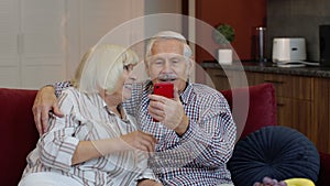 Grandmother and grandfather making video call online on mobile phone at home. Smiling senior couple