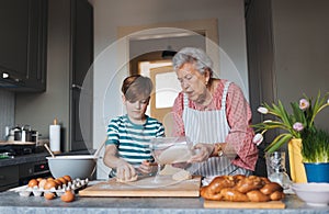 Grandmother with grandson preparing traditional easter meals, kneading dough for easter cross buns. Passing down family