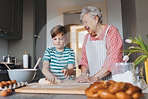 Grandmother with grandson preparing traditional easter meals, kneading dough for easter cross buns. Passing down family