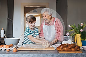 Grandmother with grandson preparing traditional easter meals, kneading dough for easter cross buns. Passing down family