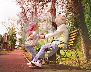 Grandmother with her cheerful granddaughter enjoying together in the park.  Kid is enjoying kindness and happy pastime