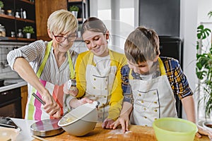 Grandmother and her grandchildren making cakes together in the home kitchen