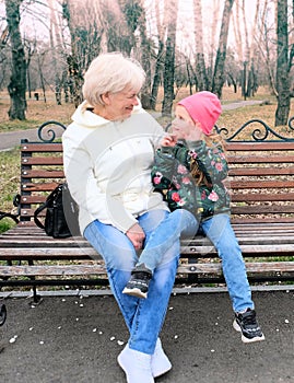 Grandmother with her granddaughter hugging and talking  sitting on a bench in the park