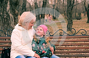 Grandmother with her granddaughter hugging and talking  sitting on a bench in the park