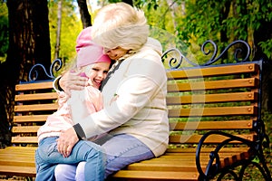 Grandmother with her granddaughter hugging and talking  sitting on a bench in the park. Toned