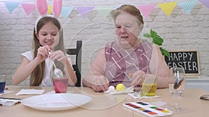 Grandmother and her granddaughter painting Easter eggs at home