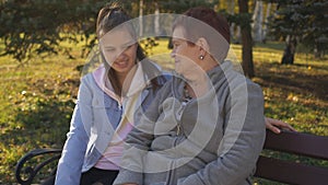 Grandmother with her granddaughter, a teenager sitting on a Park bench and talk.