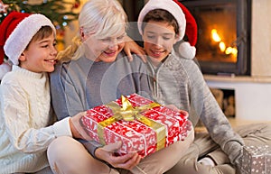 Grandmother With Her Two Grandchildren, Holding A Christmas Gift