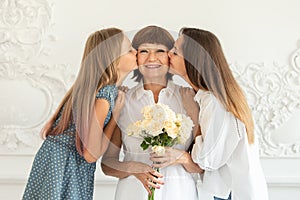 Grandmother holding flowers in hands, her daughter and granddaughter hug each other and smile