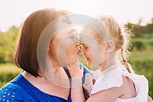 Grandmother holding granddaughter on her arms and kissing nose