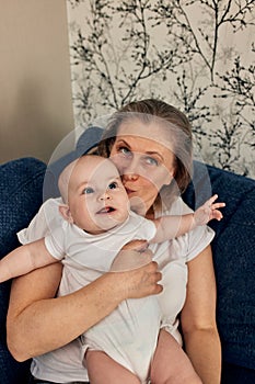 grandmother hugs and plays with her little grandson, sitting on a blue sofa in a bright room. Happy loving family.