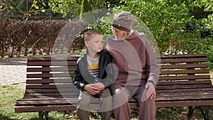 A grandmother kisses and hugs her grandson while sitting on a bench in a park.