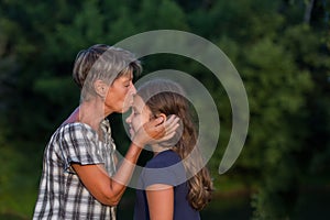 Grandmother kissing litlle granddaugther outdoor at evening photo