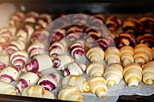 Grandmother making handmade tasty butter rolling cookies with fruit and berry jam on oven tray before baking at kitchen