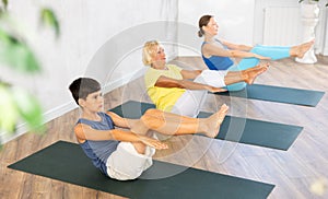 Grandmother, mother and teen son do sitting boat pose Paripurna Navasana in gym