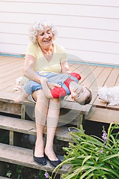 Grandmother playing with grandson boy on porch at home backyard. Bonding of relatives and generation communication. Old woman with