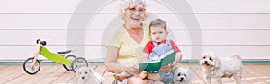 Grandmother reading book to grandson boy at home backyard. Bonding of relatives and generation communication. Old woman with baby