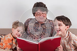 Grandmother reads a book for grandchildren. The children are laughing