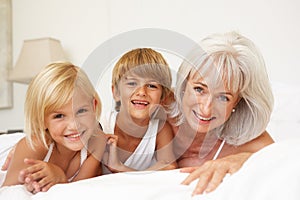 Grandmother Relaxing On Bed With Grandchildren