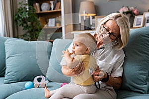 Grandmother retired woman doctor pediatric using stethoscope listening her grandson or granddaughter, young baby child lungs to