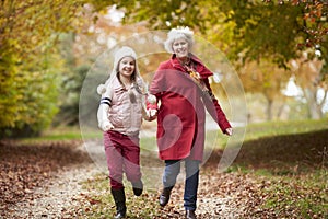 Grandmother Running Along Autumn Path With Granddaughter