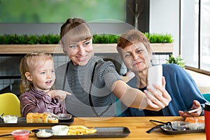 Grandmother`s daughter and granddaughter are photographed on the phone in a cafe.