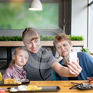 Grandmother`s daughter and granddaughter are photographed on the phone in a cafe.