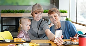 Grandmother`s daughter and granddaughter are photographed on the phone in a cafe.