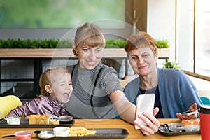 Grandmother`s daughter and granddaughter are photographed on the phone in a cafe.