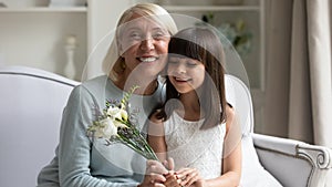 Grandmother sit on couch with little granddaughter with flowers