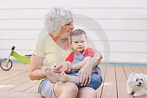 Grandmother sitting with grandson boy on porch at home backyard. Bonding of relatives and generation communication. Old woman with